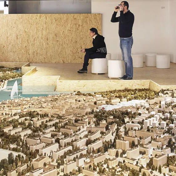 Maquette détaillée d’une ville avec de l’eau, entourée de personnes observant et prenant des photos.