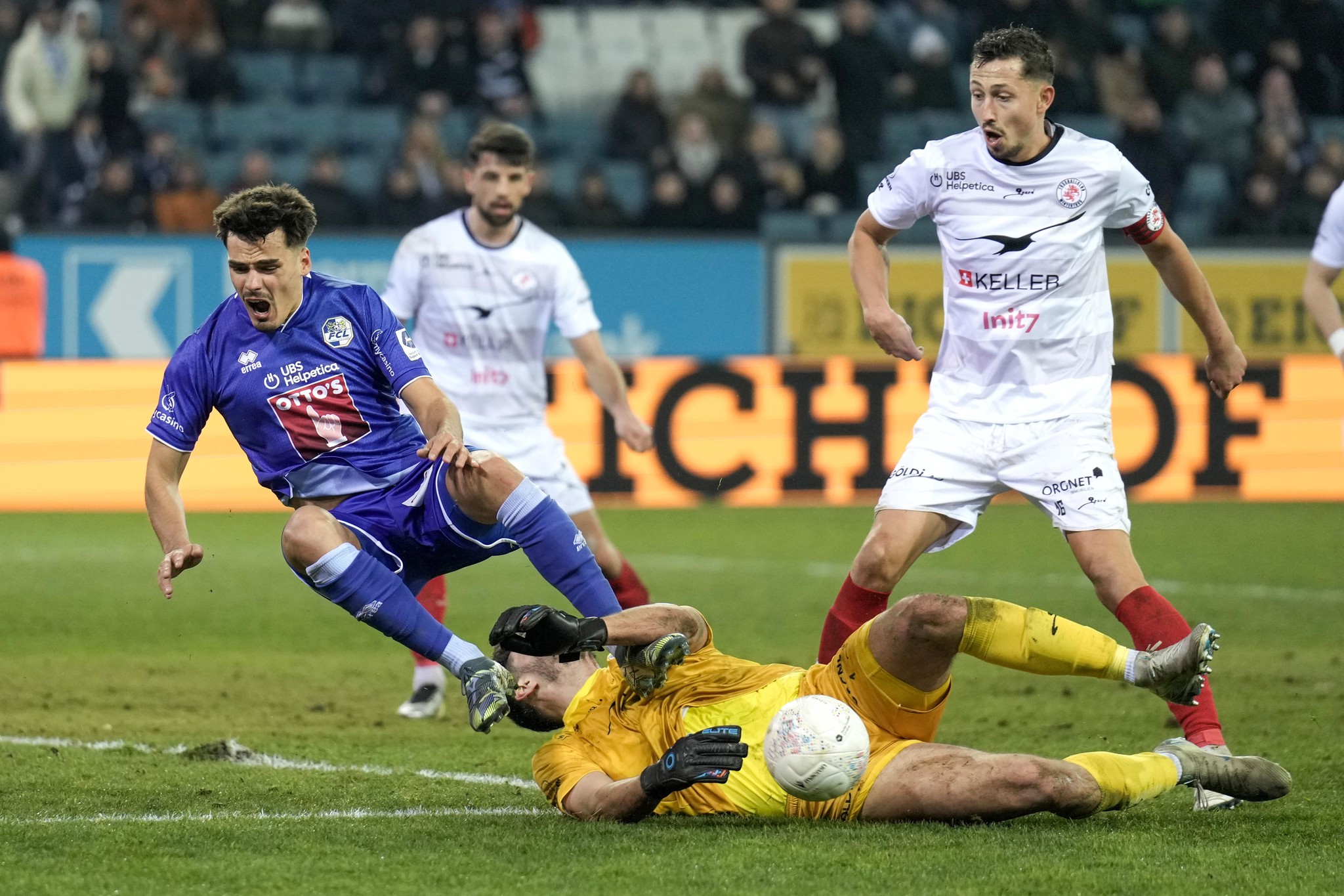 Donat Rrudhani vom FC Luzern wird im Spiel gegen FC Winterthur am 09.02.2025 von Torhüter Stefanos Kapino zu Fall gebracht, was zu einem Elfmeter führt. Andere Spieler beobachten die Szene aufmerksam.