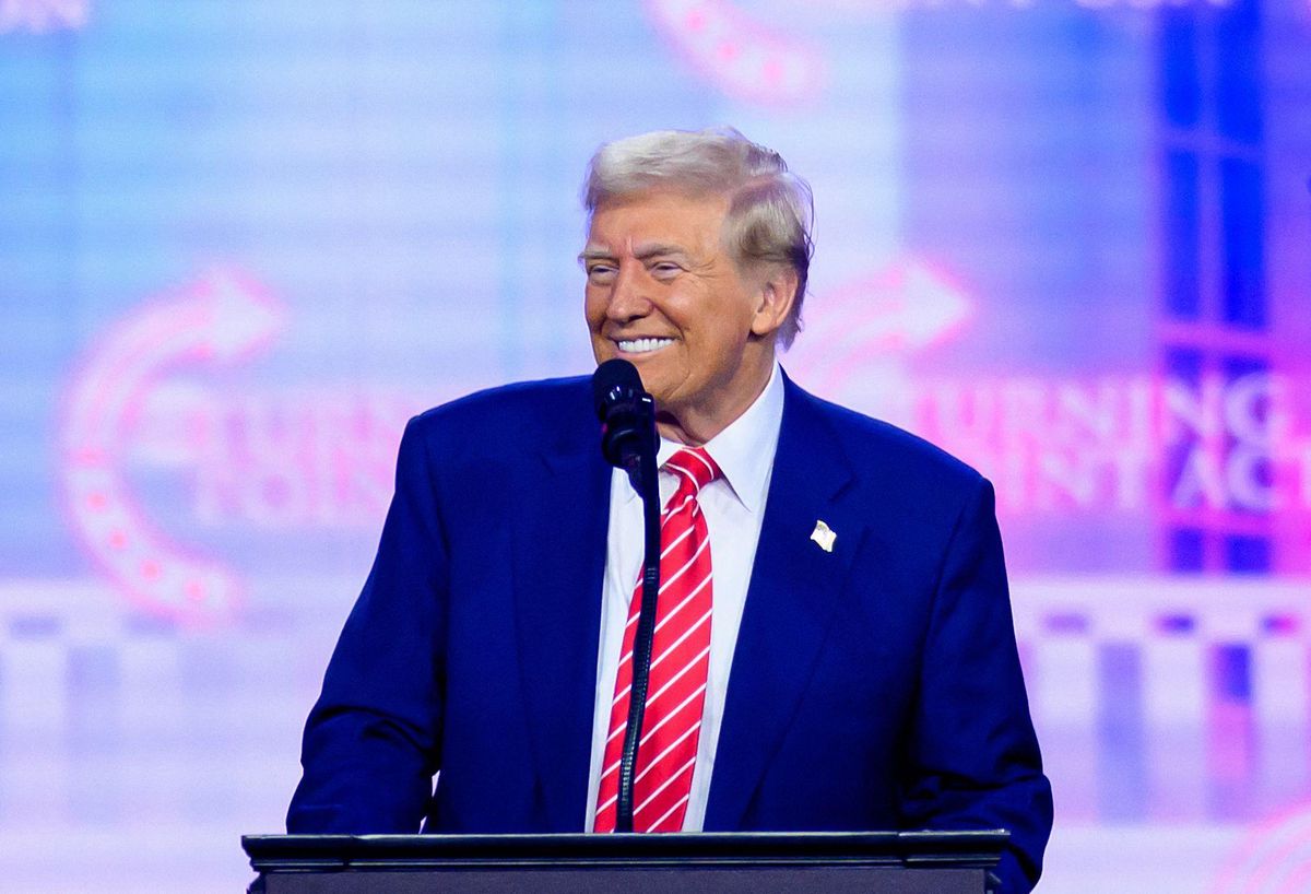 Donald Trump parlant lors du AmericaFest 2024 à Phoenix, souriant derrière un podium.