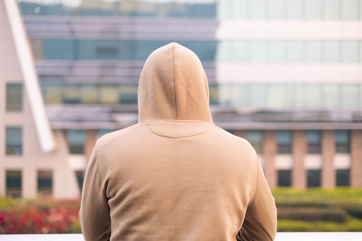 A color image shows a man in a hoodie gazing at buildings from a balcony.