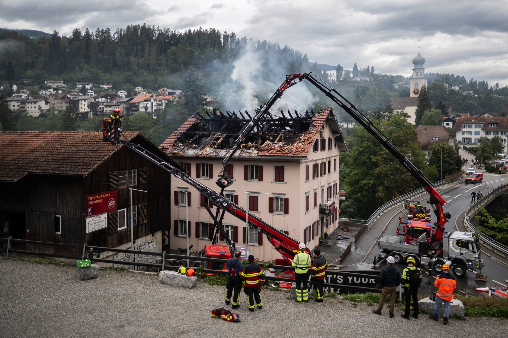 Ausgebranntes Haus in Thusis nach Grossbrand: Feuerwehrleute und Löschfahrzeuge im Einsatz, Dach zerstört, Rauch steigt auf.