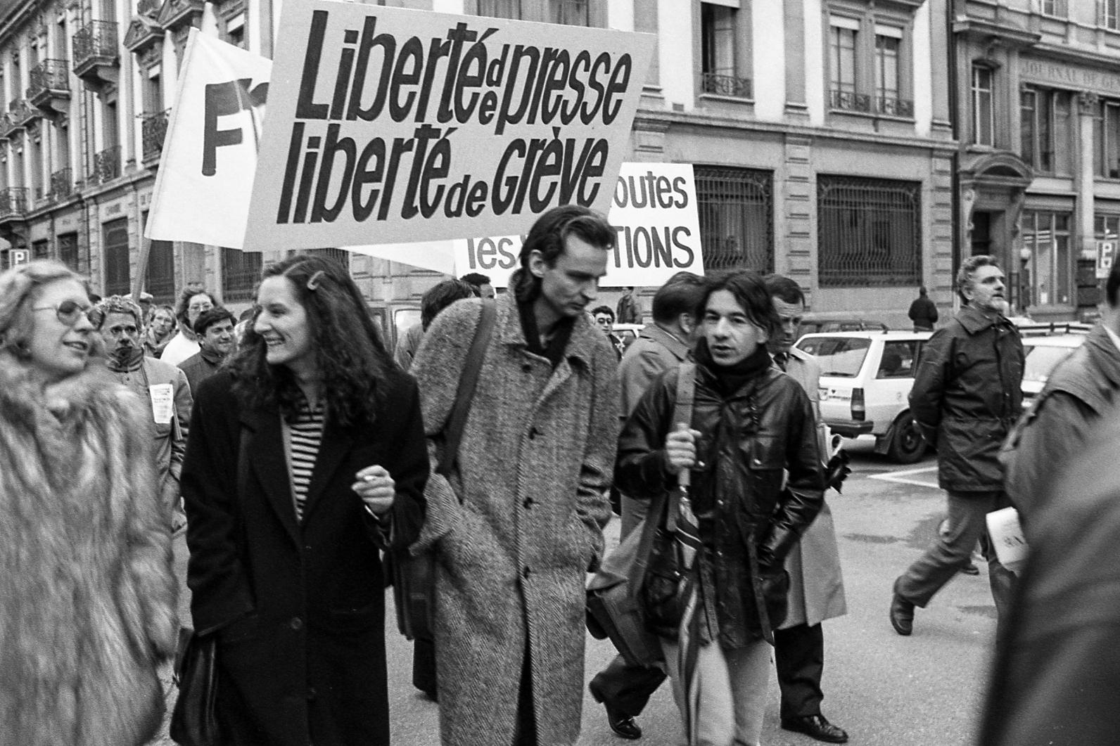 Manifestation dans une rue avec des personnes portant des pancartes proclamant la liberté de presse et de grève.