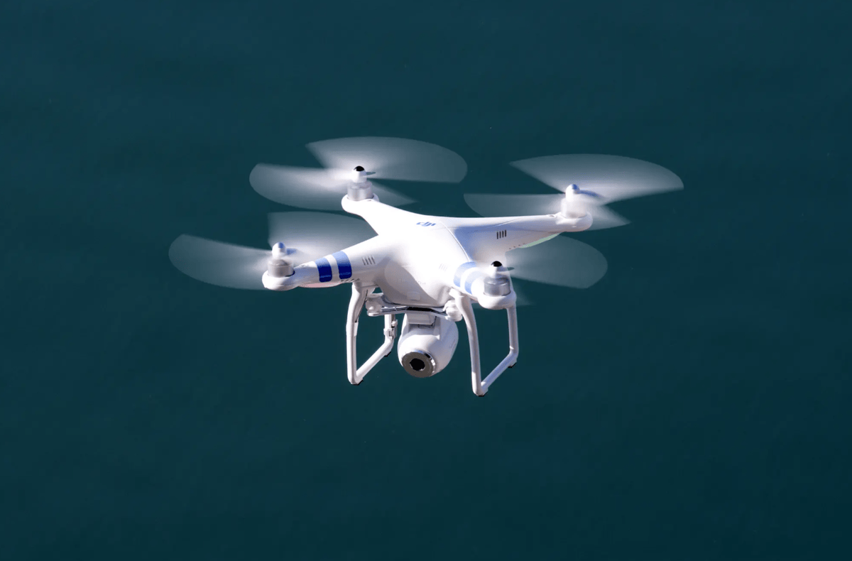 Un drone quadricoptère blanc volant au-dessus d'une étendue d'eau sombre.