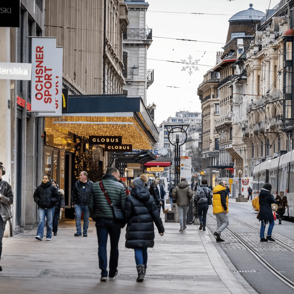Rue commerçante animée à Genève avec des passants, des tramways et des boutiques comme Bershka et Globus.