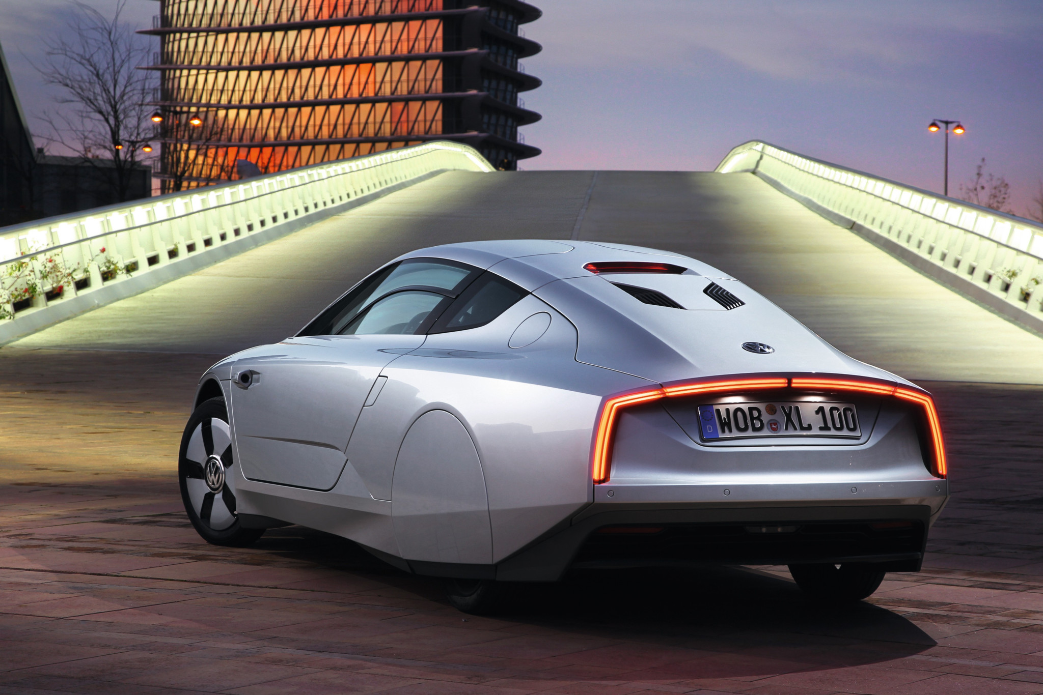 VW XL1 in Silber von hinten, Kennzeichen WOB-XL 100, vor moderner Architektur bei Abenddämmerung, Kleinserie 2013