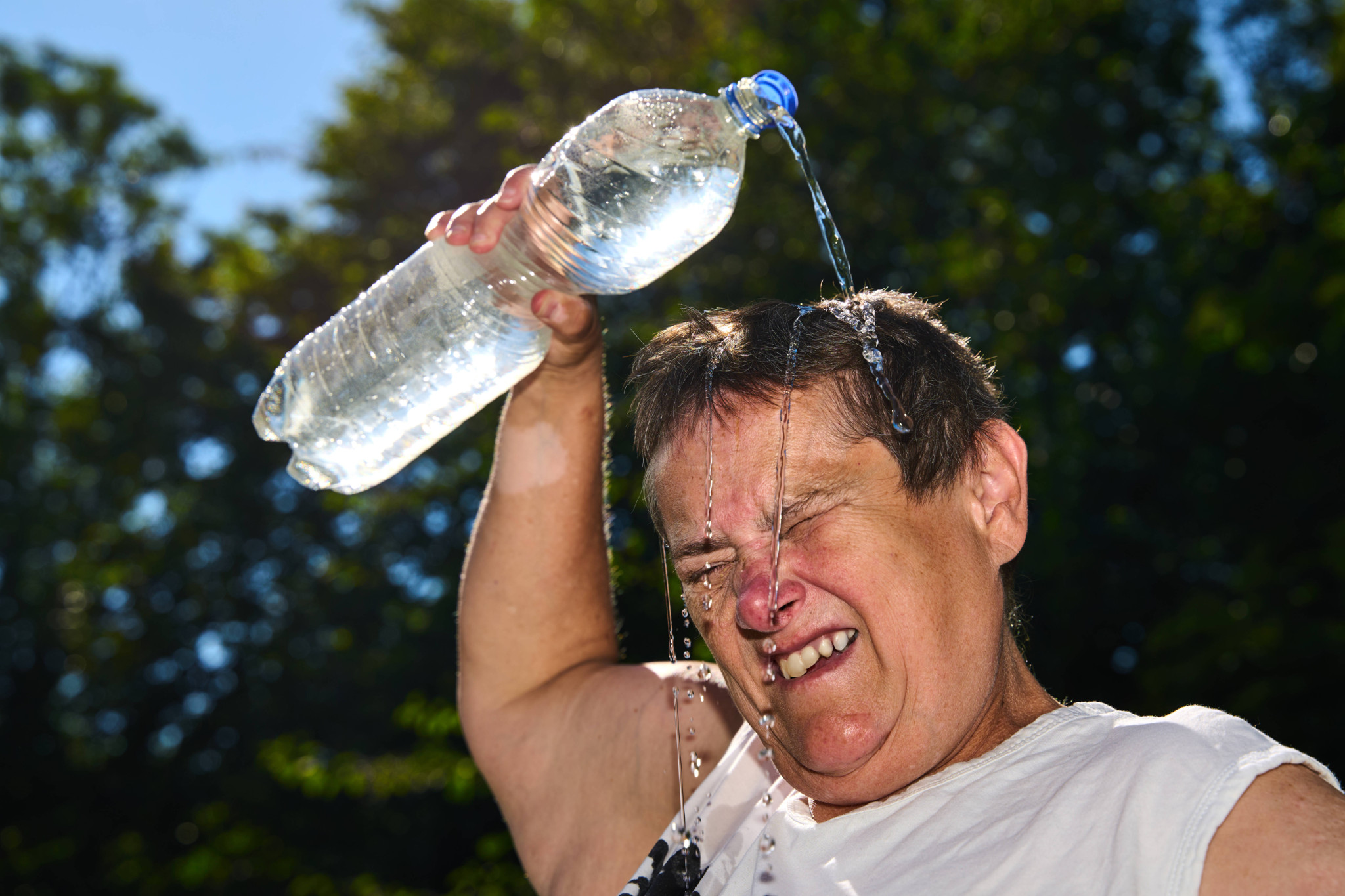 Ältere Frau übergiesst sich mit Wasserflasche zur Abkühlung während Hitzewelle in Bayern, Deutschland.