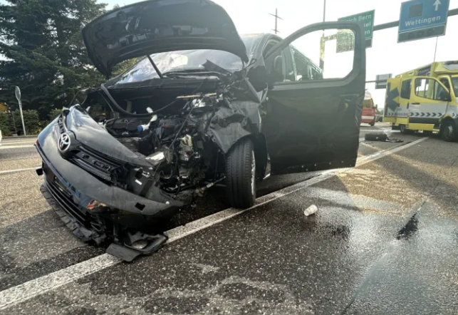 Voiture noire accidentée avec capot ouvert et ambulance en arrière-plan sur une autoroute.