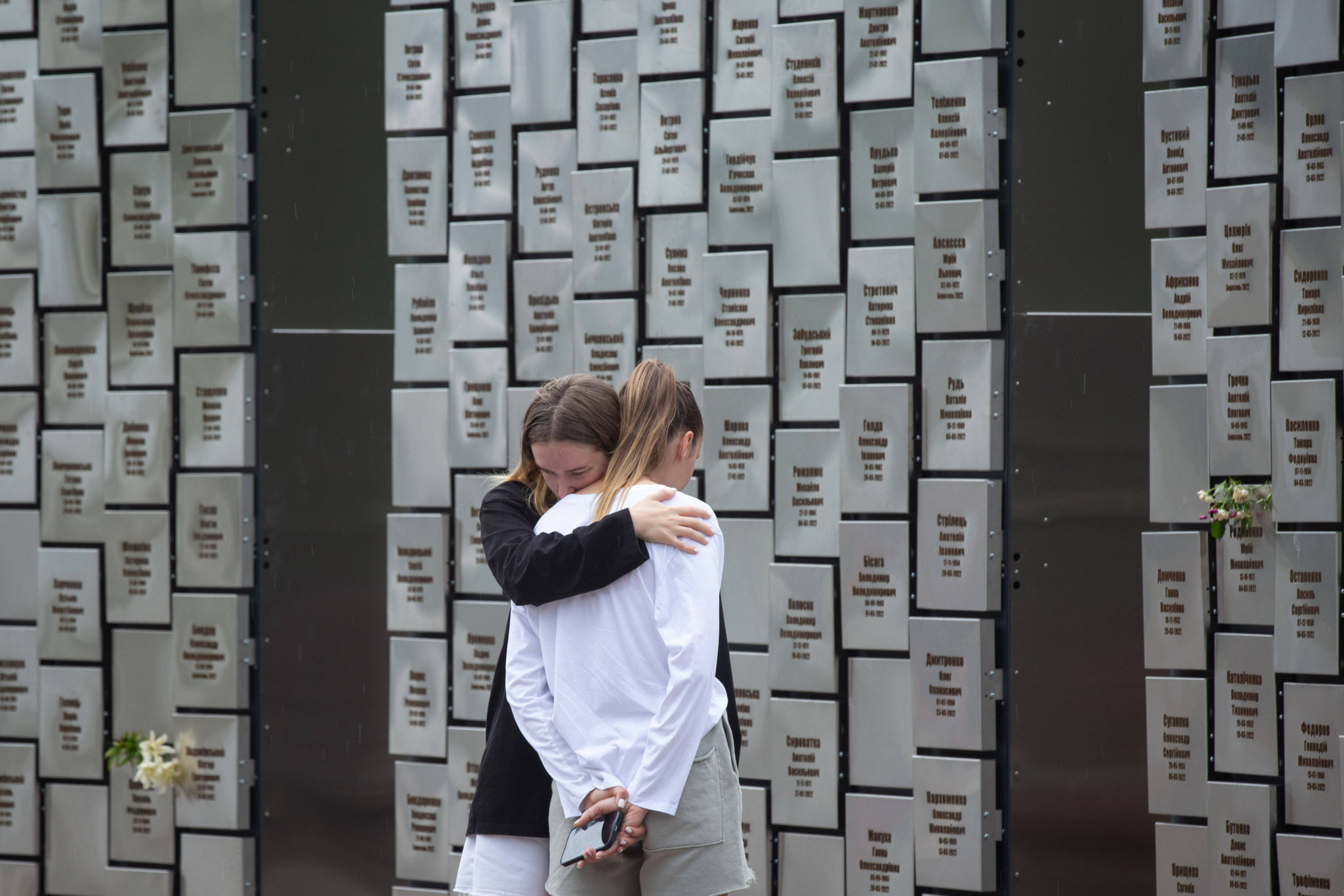 Zwei Mädchen trauern vor einem Denkmal in Butscha, Ukraine, mit den Namen von 501 zivilen Opfern des Krieges. Juli 2023.
