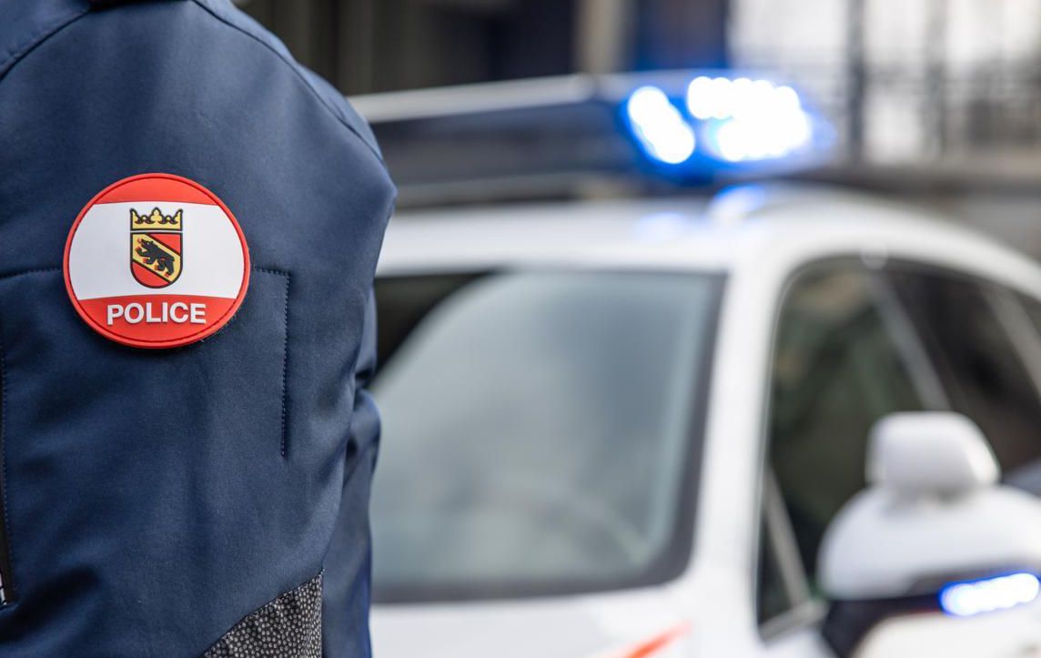 Polizeibeamter in Uniform neben einem Polizeiauto mit eingeschaltetem Blaulicht in einer städtischen Umgebung.