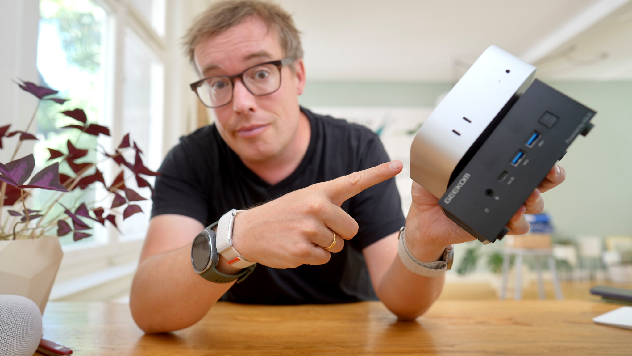 Mann mit Brille zeigt auf einen kleinen Mini-PC mit USB-Anschlüssen, den er in der Hand hält.