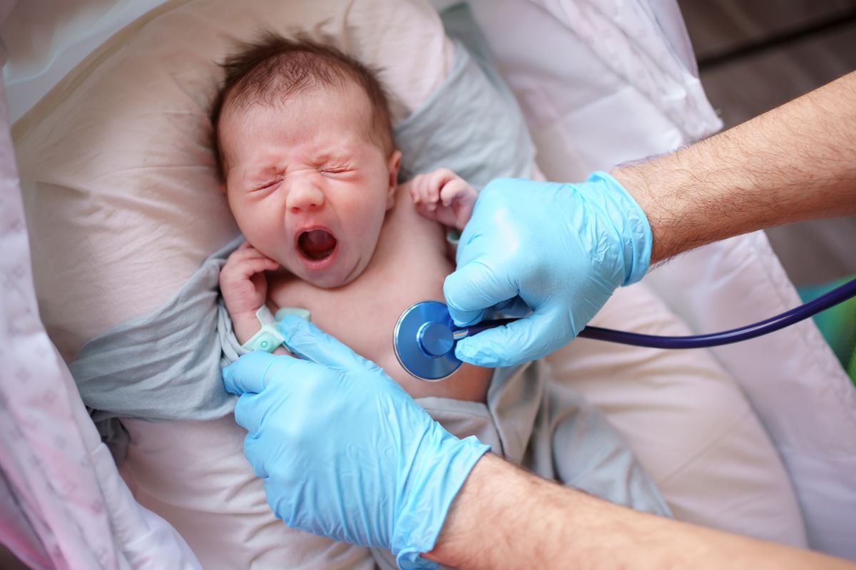 Homme portant des gants médicaux bleus écoute un bébé avec un stéthoscope
