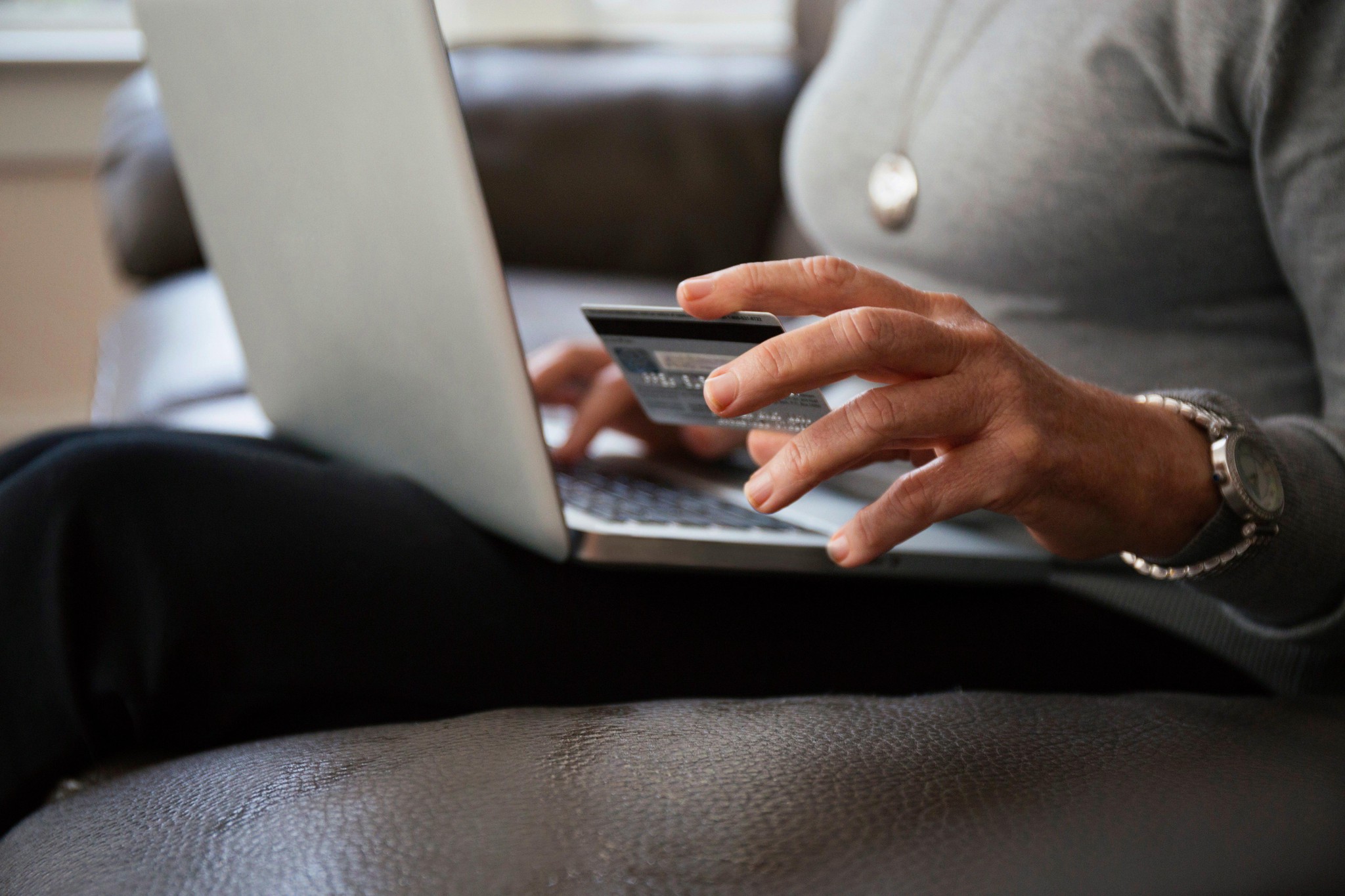 Nahaufnahme einer älteren Frau, die zu Hause online einkauft. Sie hält eine Kreditkarte in der Hand und sitzt vor einem Laptop.