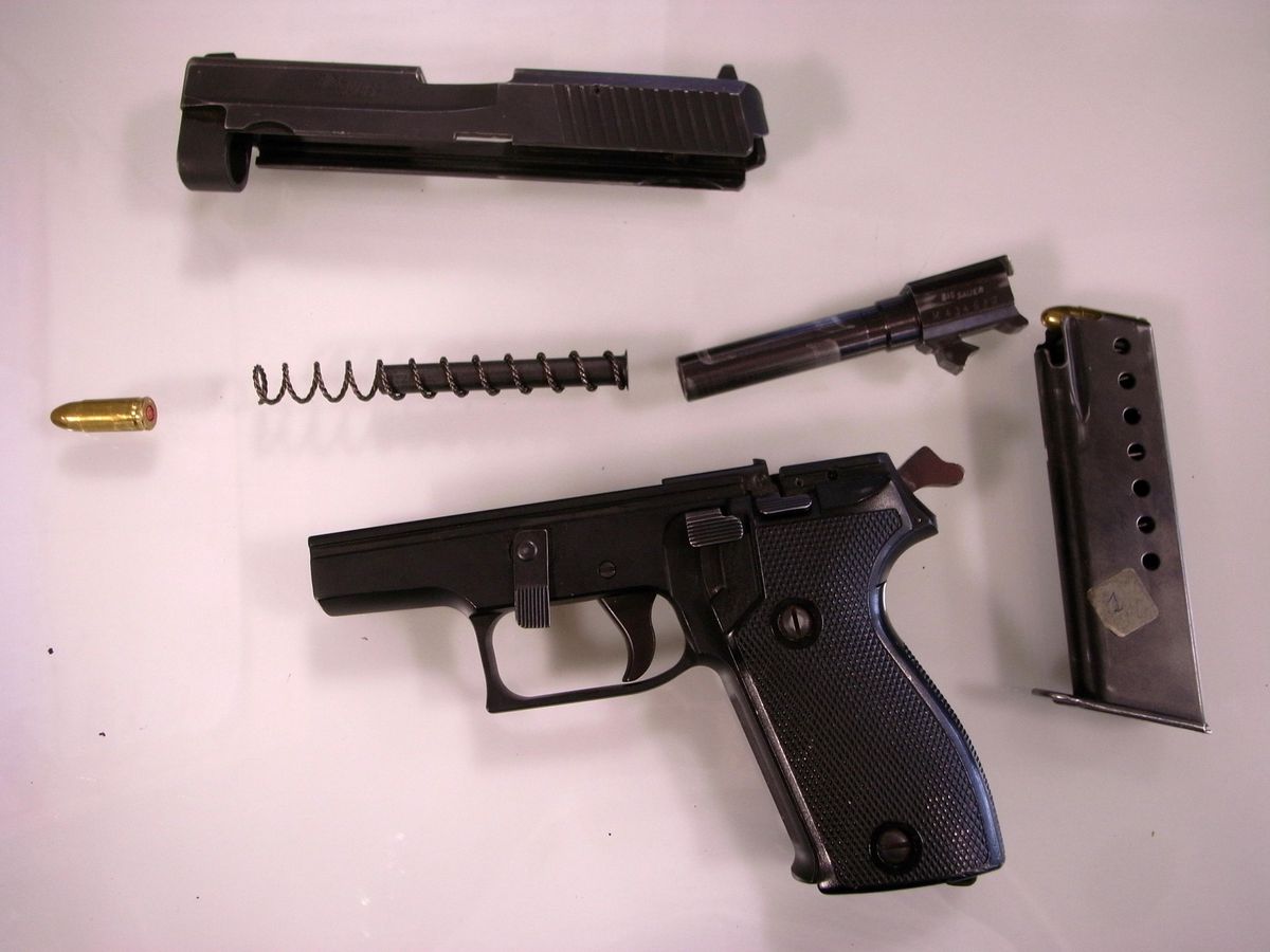 Différentes pièces détachées d’une arme à feu, y compris un pistolet démonté, une balle, et un chargeur, illustrant la difficulté de la traçabilité des armes en Suisse.