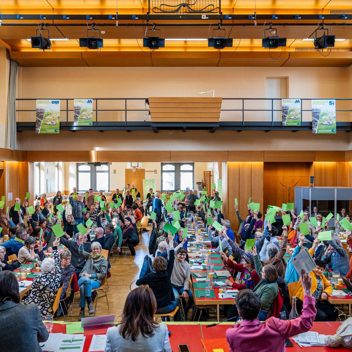 Participants dans une salle de conférence levant des cartes vertes lors d’une réunion avec des tables alignées et des personnes engagées.