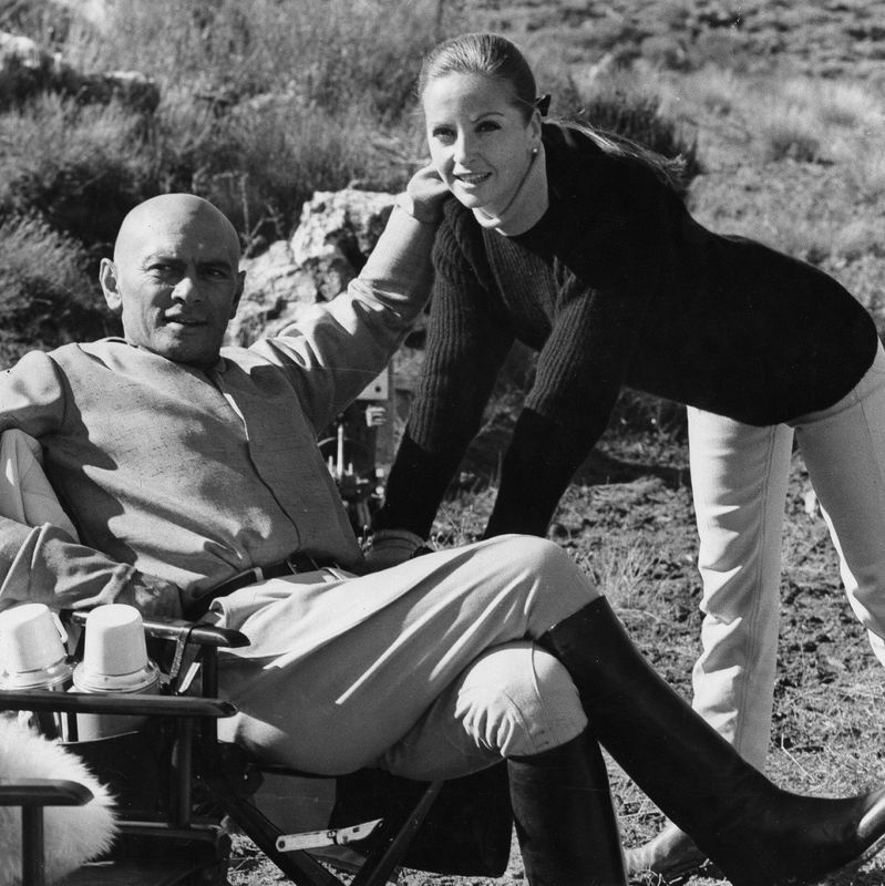 Yul Brynner, acteur, avec sa femme Doris Kleiner en été 1960, assis en extérieur, souriant.