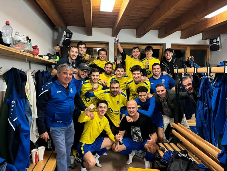 Männermannschaft in gelben Fussballtrikots feiert in einer Umkleidekabine, lächelt und posiert für ein Foto.