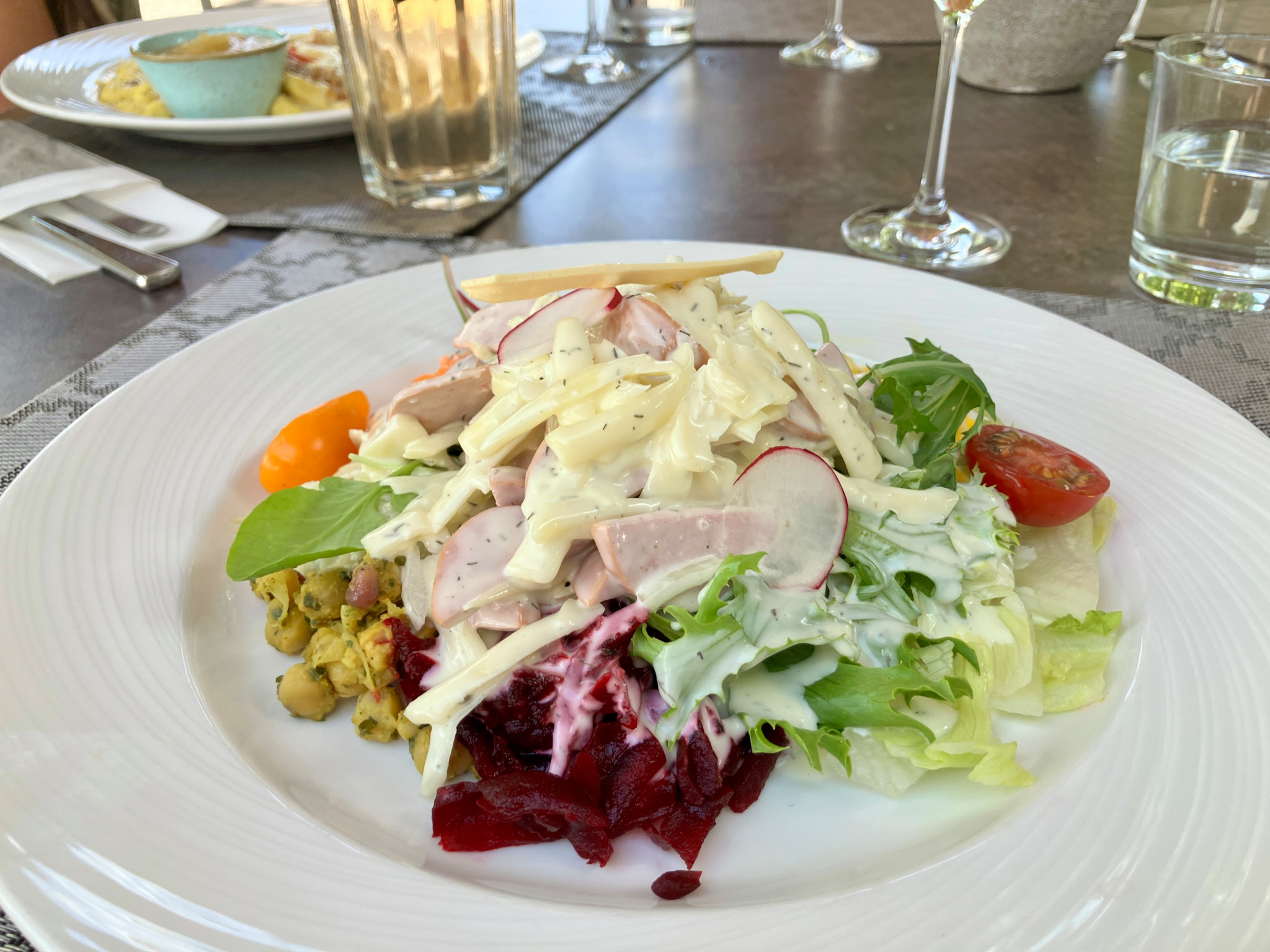 Bunter Salatteller mit Käse, Radieschen, Tomaten, Randen und Fleischstreifen auf weissem Teller, serviert in einem Restaurant.