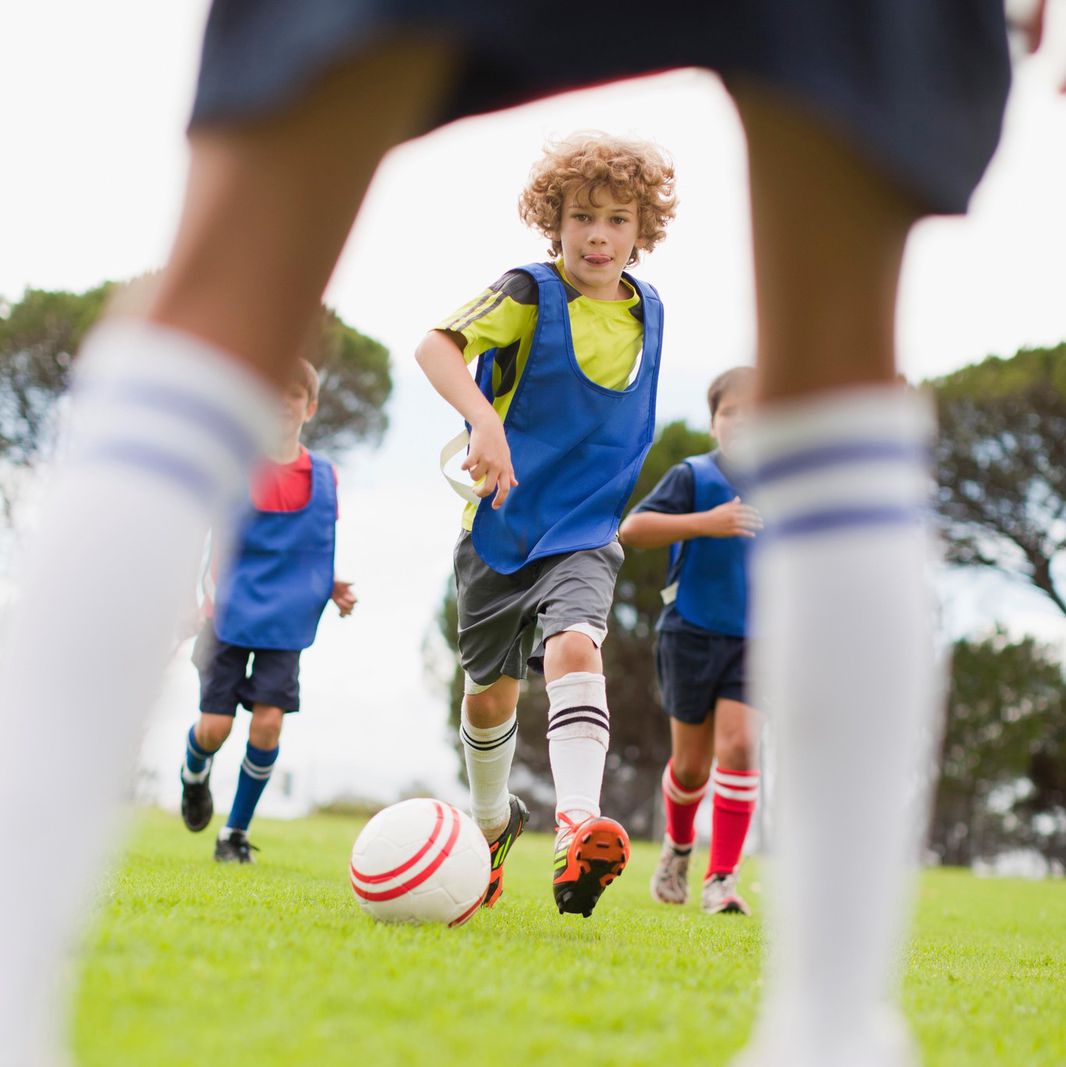 Enfants jouant au football dans un parc, portant des gilets bleus et des protège-tibias, concentrés sur le ballon.