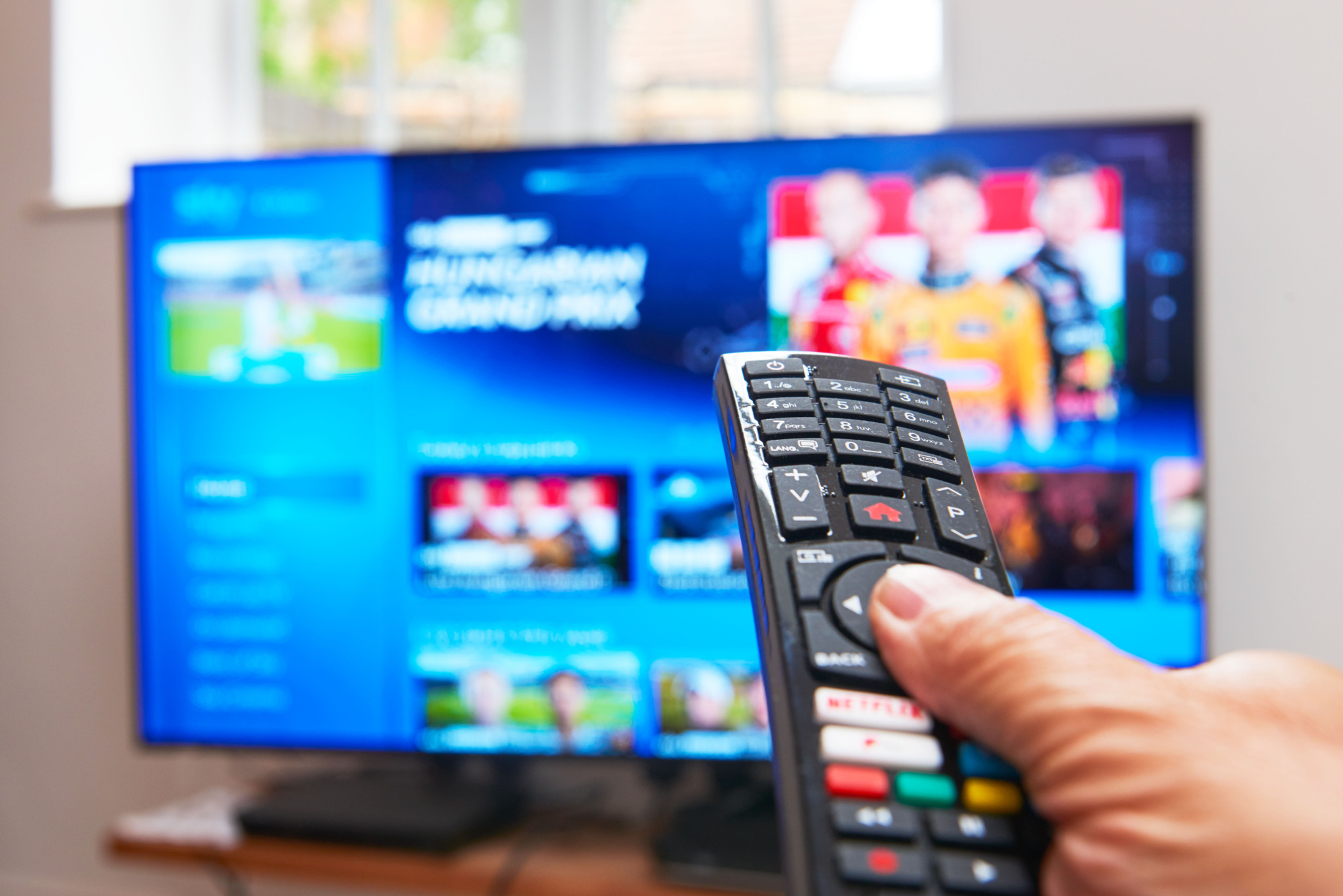 Une main tenant une télécommande noire pointée vers un téléviseur intelligent affichant un menu de streaming avec du contenu sportif.