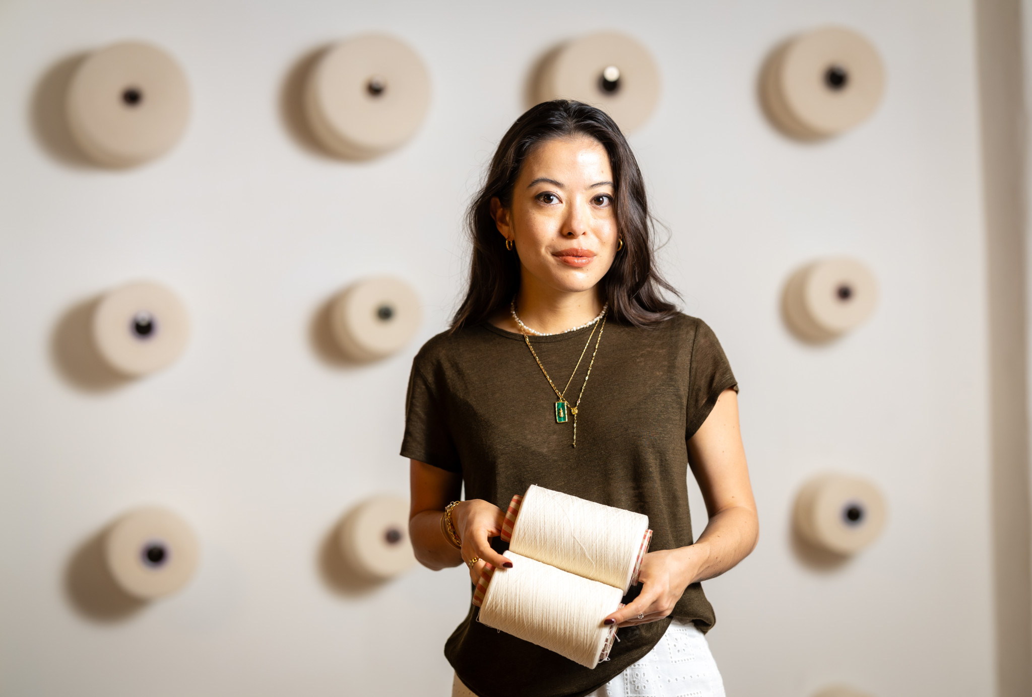 Annabelle Hutter hält recyceltes Garn, umgeben von Textilspulen an einer Wand in Zürich. Innovation durch Säntis Textiles.