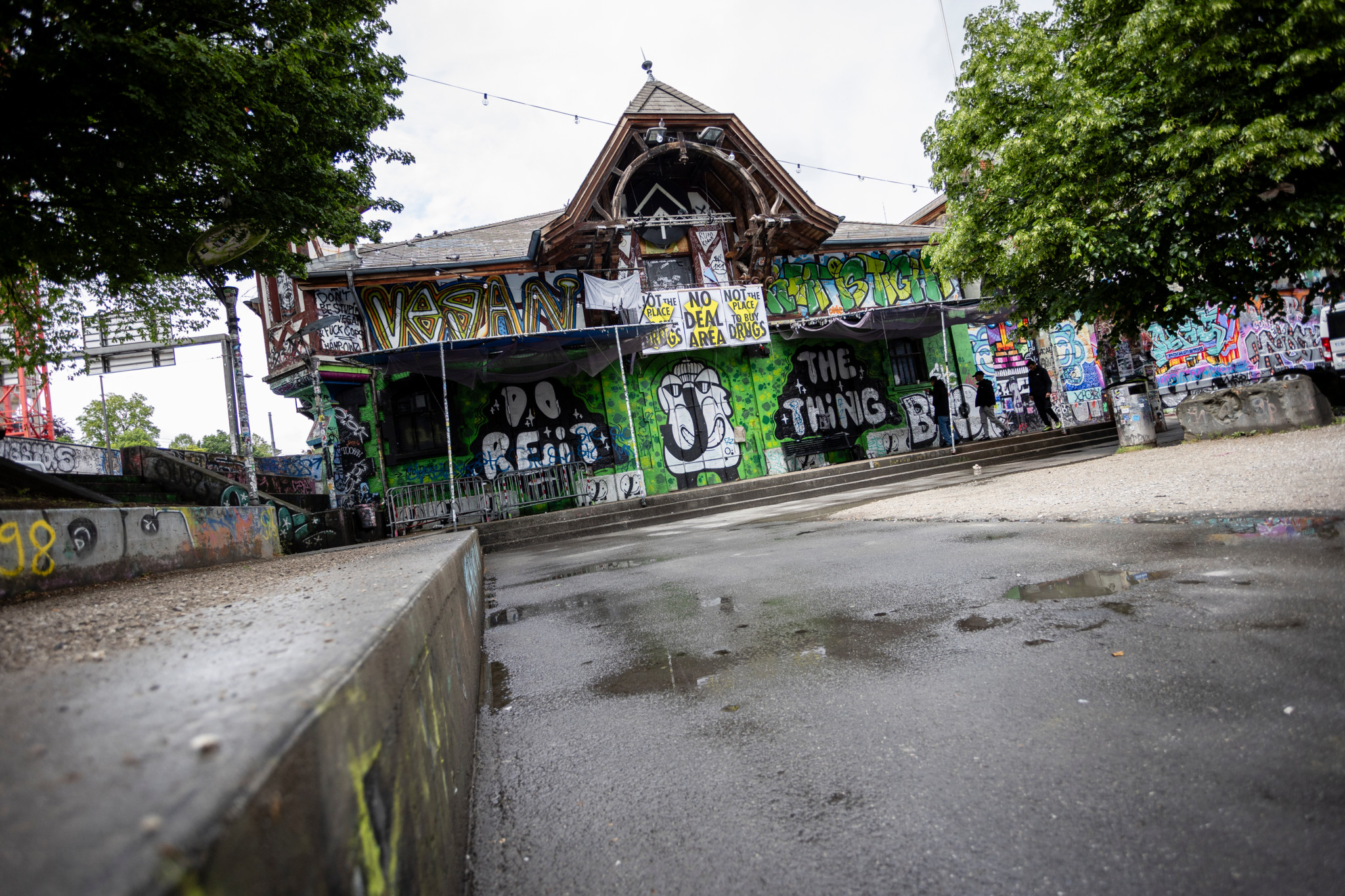Aussenansicht der Reitschule Bern mit bunten Graffiti bedeckten Wänden und nassem Vorplatz, Kulturzentrum im Fokus nach abgesagter Filmvorstellung.