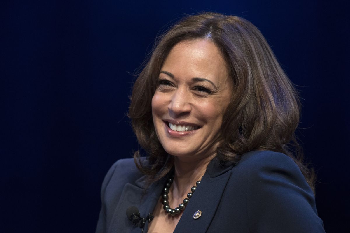 Kamala Harris, souriante et portant un costume bleu marine et un collier de perles noires sur un fond bleu foncé.