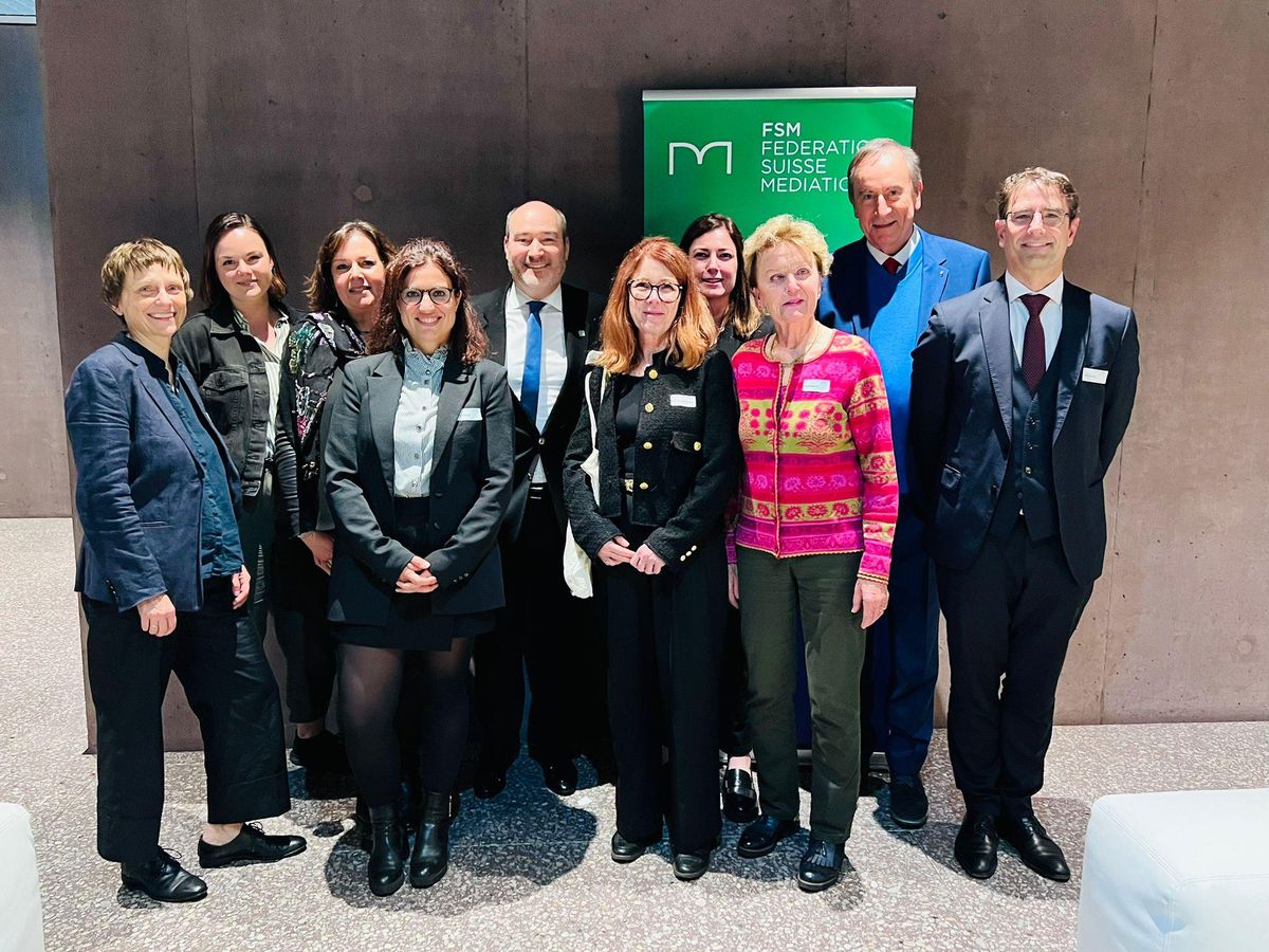 Groupe de personnes debout devant une bannière de la Fédération Suisse des Médiateurs, habillées en tenues formelles.