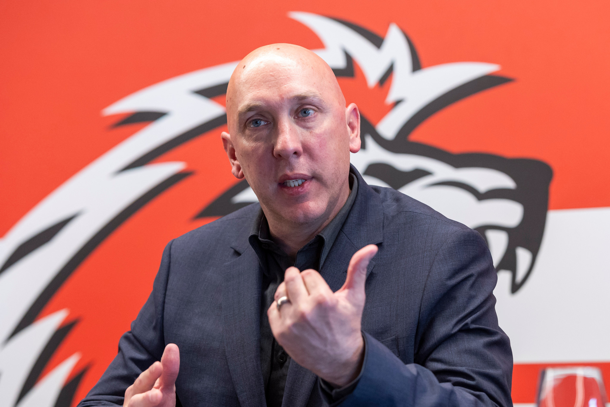 John Fust lors d’une conférence de presse de Lausanne HC, devant un fond rouge avec un motif de lion, mars 2024.
