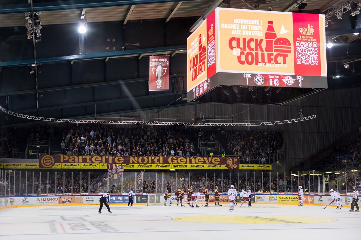 Vue d'ensemble de la patinoire des Vernets à Genève lors d'un match de hockey sur glace entre le Genève-Servette Hockey Club et les SC Rapperswil-Jona Lakers, avec le public, une bannière de champion de la CHL et l'écran Videotron. 