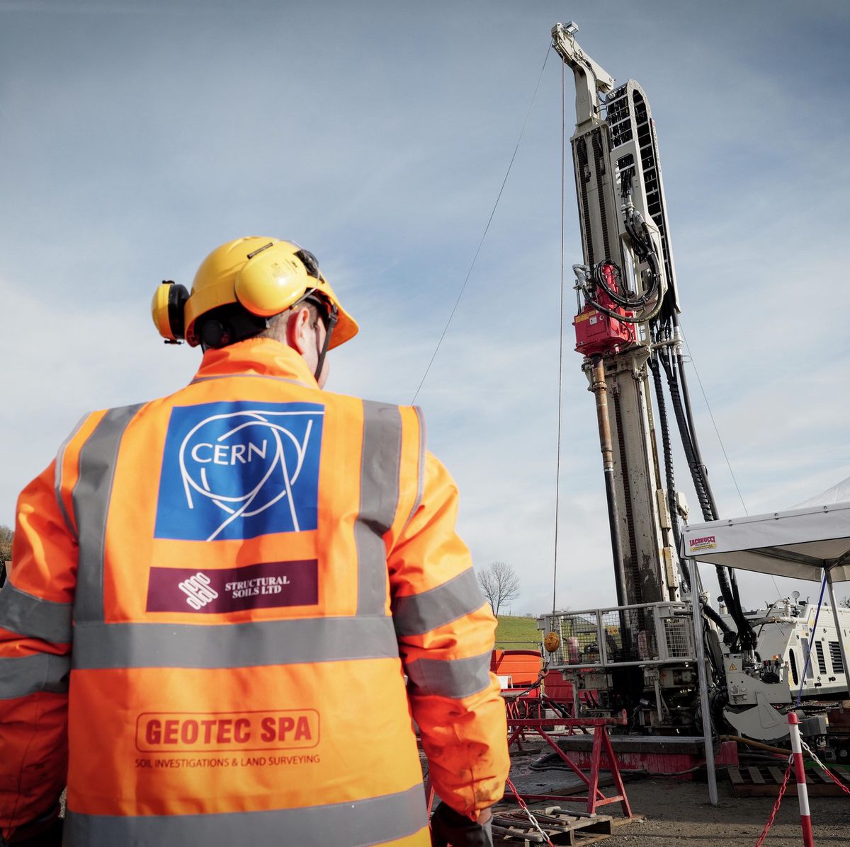 Un ingénieur porte un gilet siglé CERN lors d’une étude de faisabilité pour un Futur collisionneur circulaire en Haute-Savoie, avec une foreuse en arrière-plan.