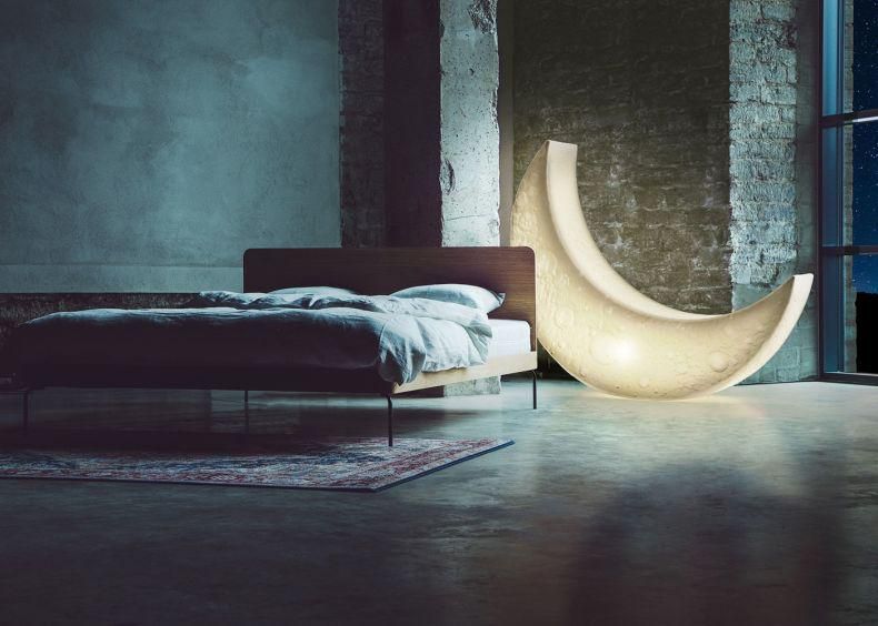 Chambre moderne avec lit minimaliste, mur en béton brut et lampe en forme de demi-cercle éclairée.