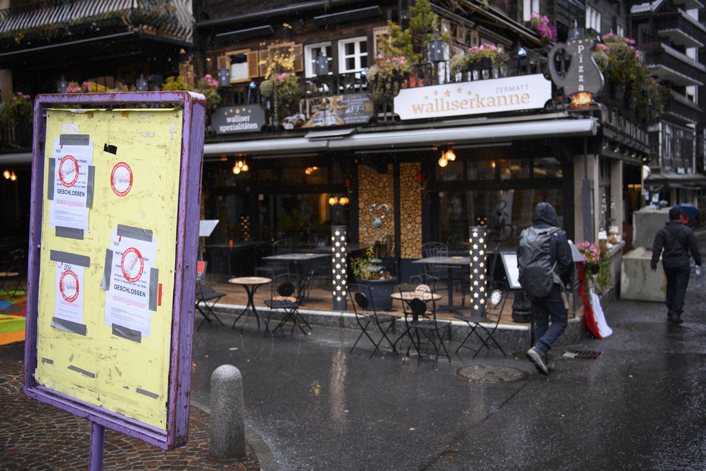 Des passants devant le restaurant ’Walliserkanne’ à Zermatt, fermé et scellé avec des blocs de béton à cause de violations des lois Covid-19, avec un panneau annonçant sa fermeture.