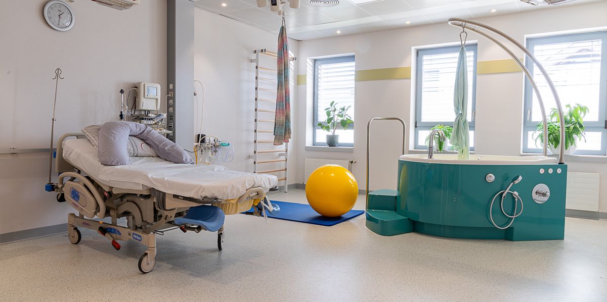 Salle de naissance moderne avec un lit d'hôpital, une piscine d'accouchement, et un ballon de yoga.