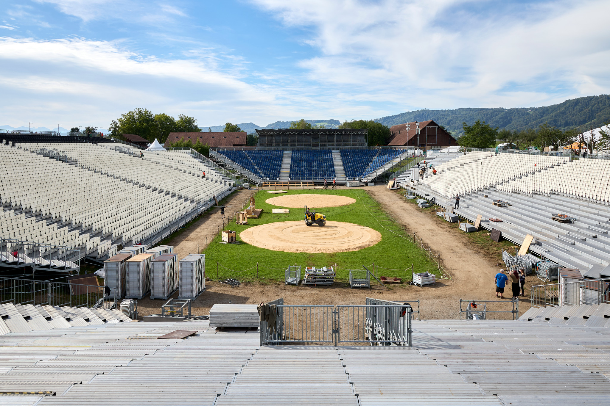 Aufbau der Arena für den Kilchberger Schwinget 2026 mit Sägemehlring und Tribünen im Freien, Berge im Hintergrund.