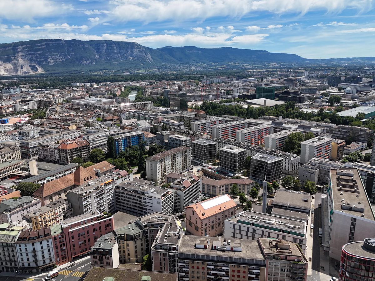 Vue aérienne de Genève capturée par drone depuis le cimetière des Rois, montrant des bâtiments et le paysage urbain avec des montagnes à l'horizon.
