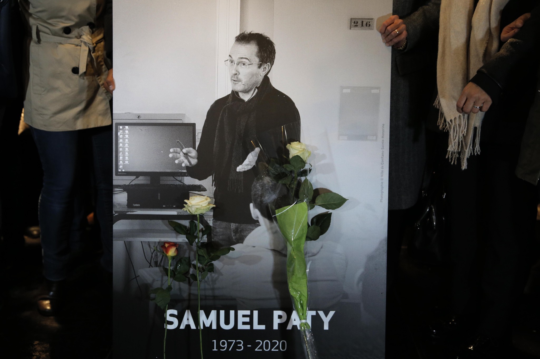 Menschen halten ein Foto von Samuel Paty mit Blumen während eines Gedenkmarsches in Conflans-Sainte-Honorine, 2020.