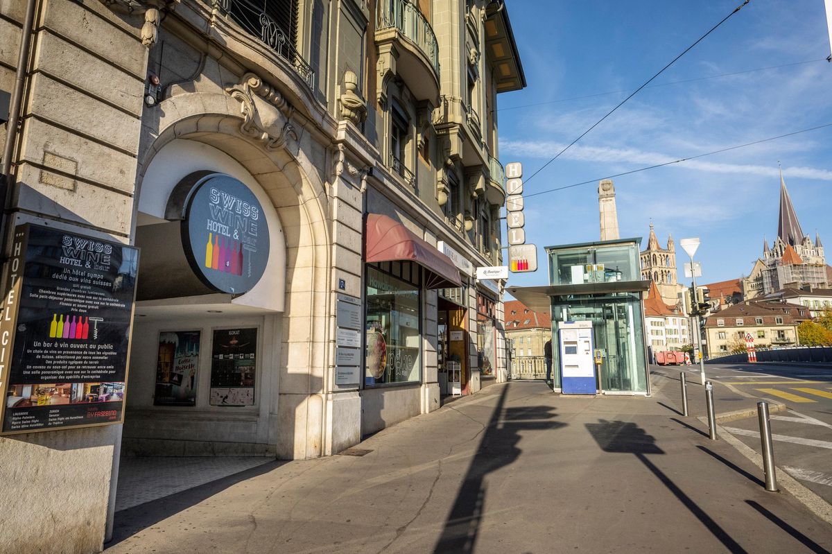Entrée du Swiss Wine Hotel & Bar à Lausanne, avec une rue ensoleillée et des bâtiments historiques en arrière-plan.