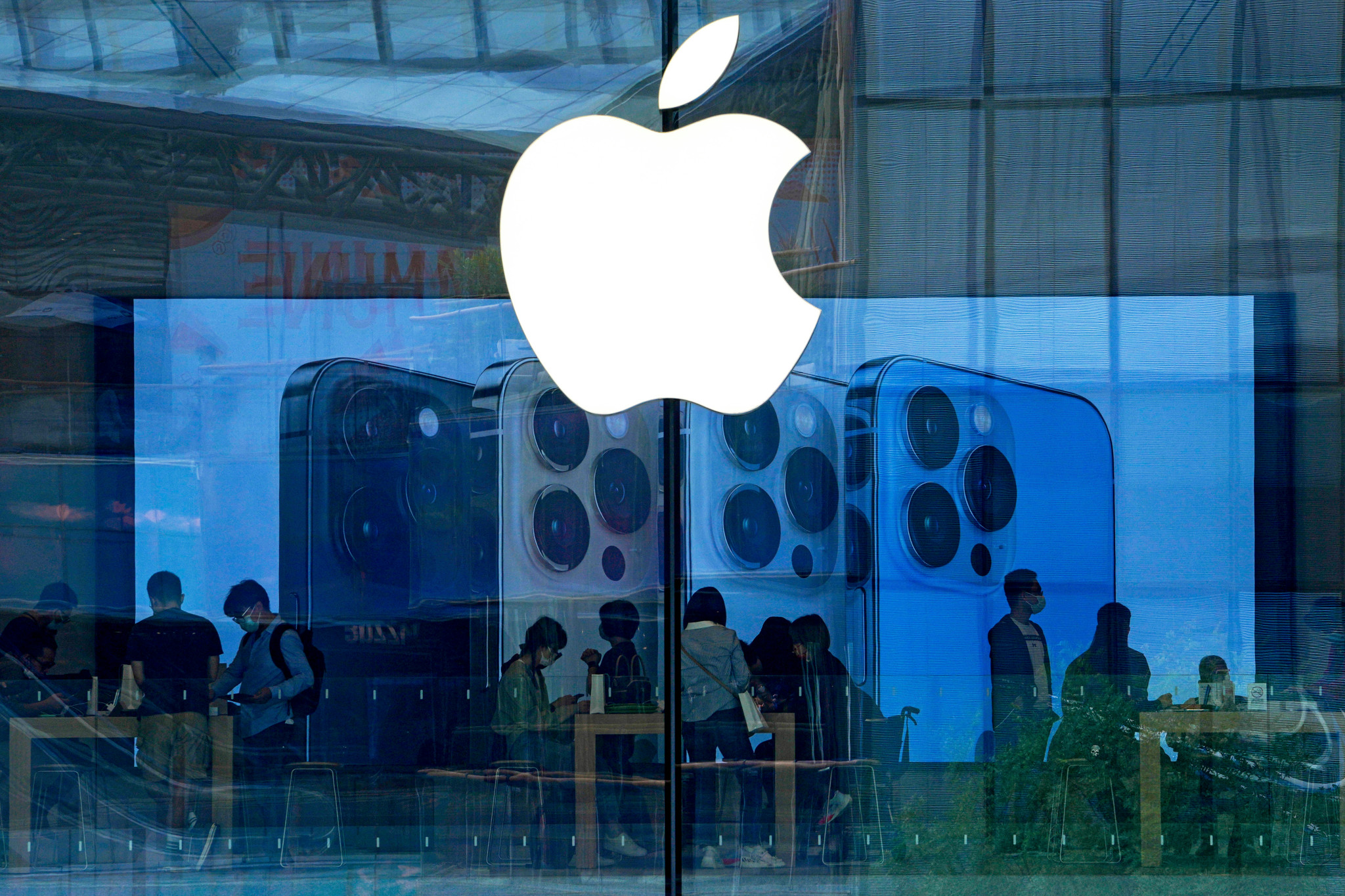 Kunden mit Masken testen iPhone 13 in einem Apple Store in Peking, Apple-Logo und iPhone-Werbung im Vordergrund.