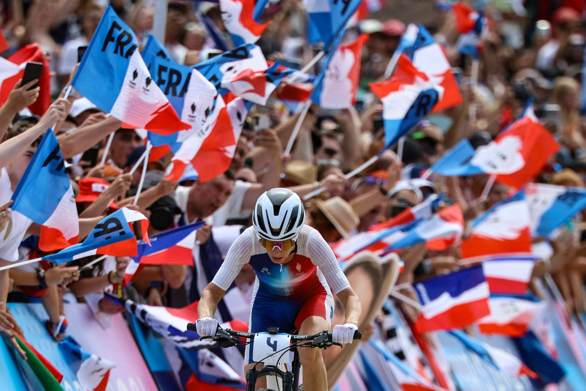 TOPSHOT - France's Pauline Ferrand Prevot cycles past spectators waving French flags as she competes in the women's cross-country mountain biking event during the Paris 2024 Olympic Games in Elancourt Hill venue in Elancourt, on July 28, 2024. (Photo by Emmanuel DUNAND / AFP)