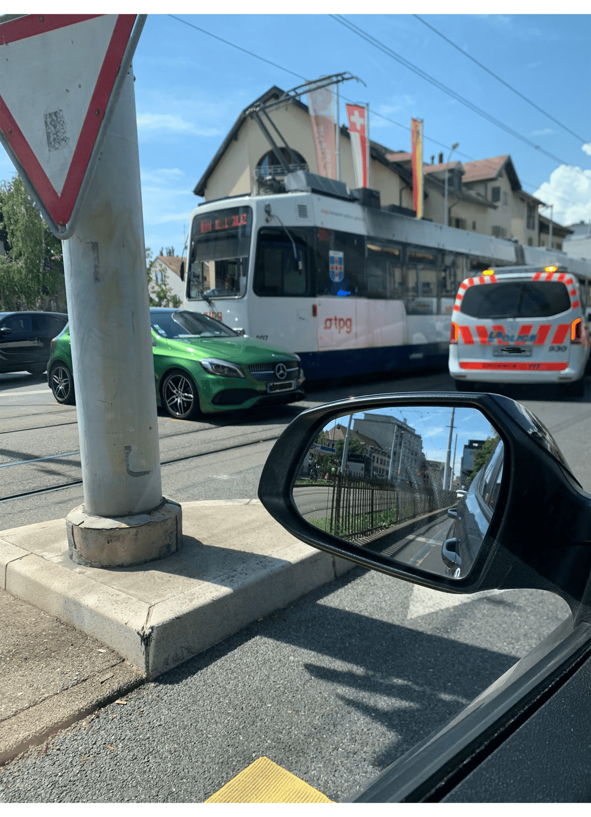 Un tramway, une ambulance et une voiture verte se rencontrent à une intersection animée à Genève.