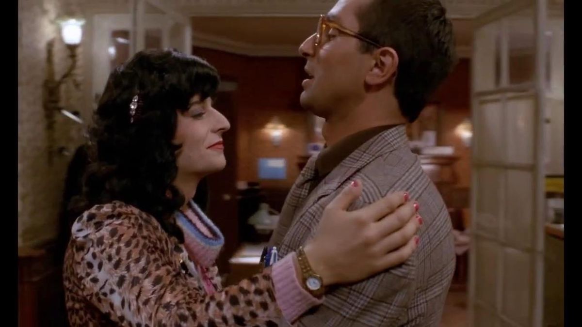 Deux personnes dans un câlin dans une pièce bien éclairée, décorée de façon chaleureuse, avec des murs en bois et des portes en verre.