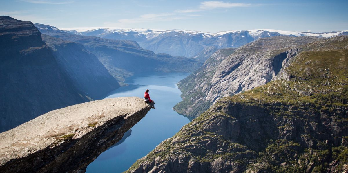 man sitting on trolltunga rock above a norwegian fjord.