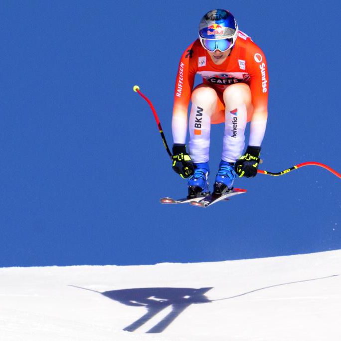 Un skieur vêtu de rouge et orange effectue un saut lors de la course de descente masculine à Wengen, Suisse, pendant la Coupe du monde de ski FIS.