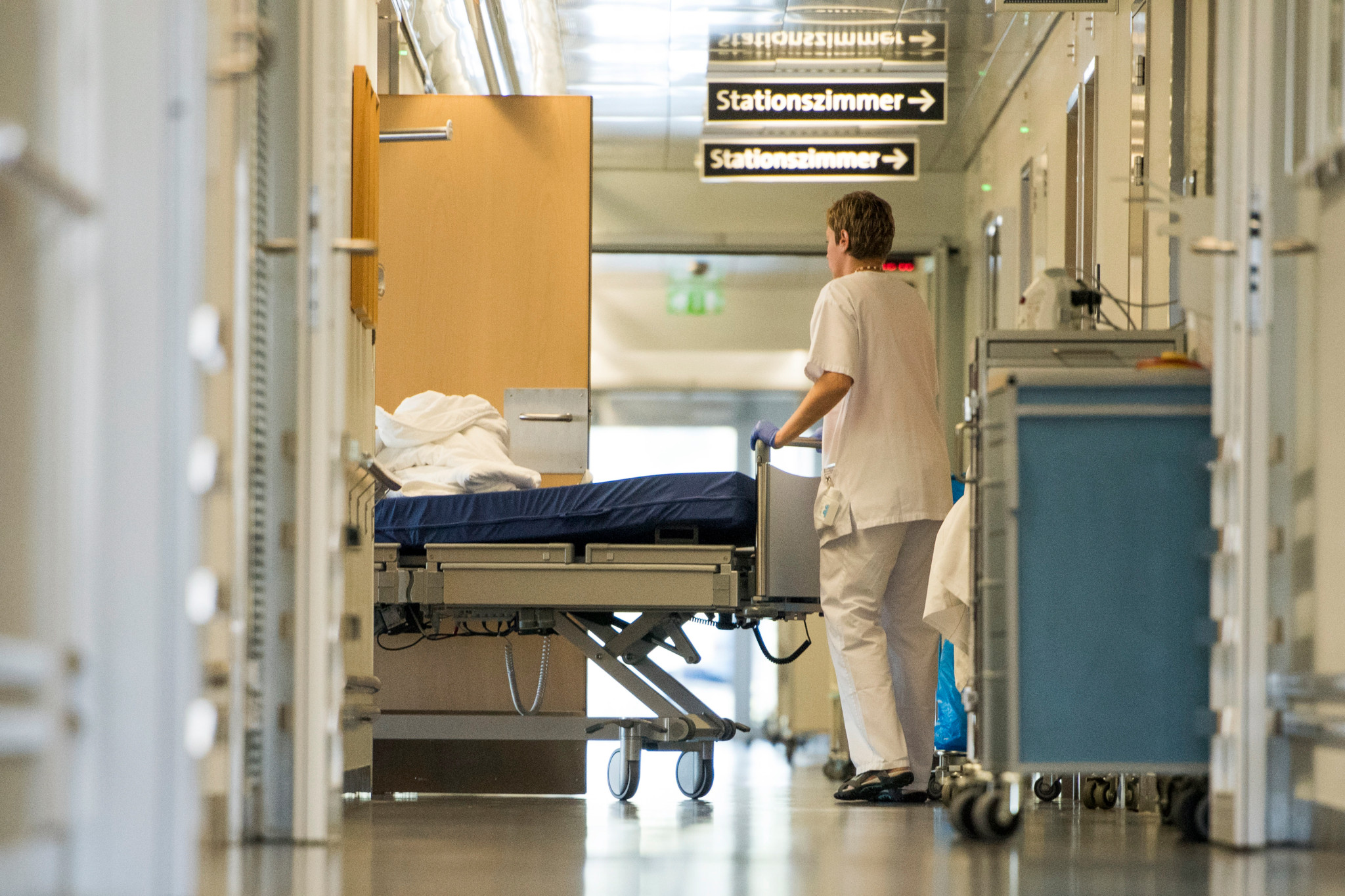 Pflegeperson schiebt ein Krankenbett durch den Korridor der Privatabteilung im Kantonsspital Winterthur, Schilder zeigen zum Stationszimmer.