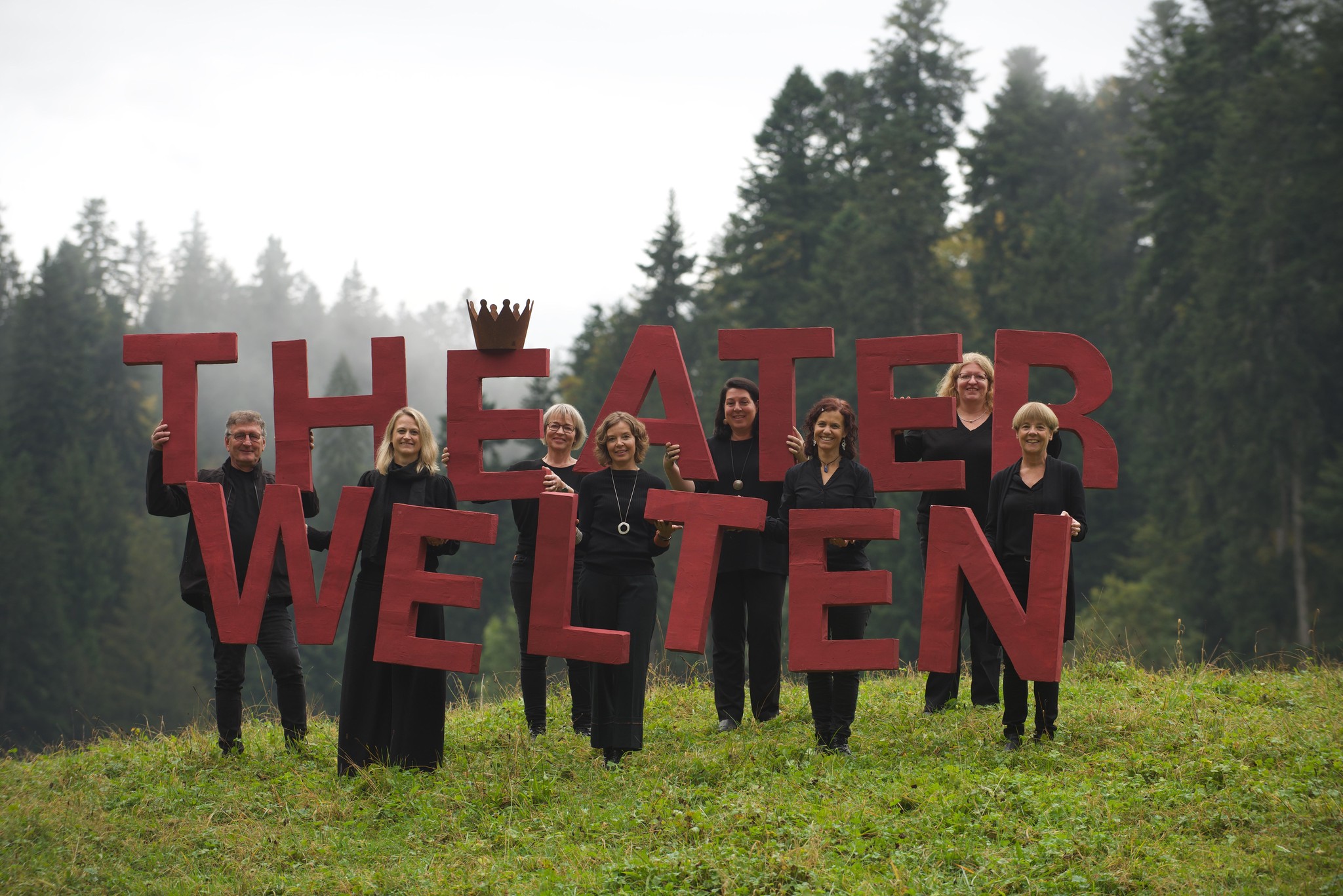 Mitglieder des neu benannten 'theaterwelten' halten Buchstaben des Namens vor einem Waldhintergrund.