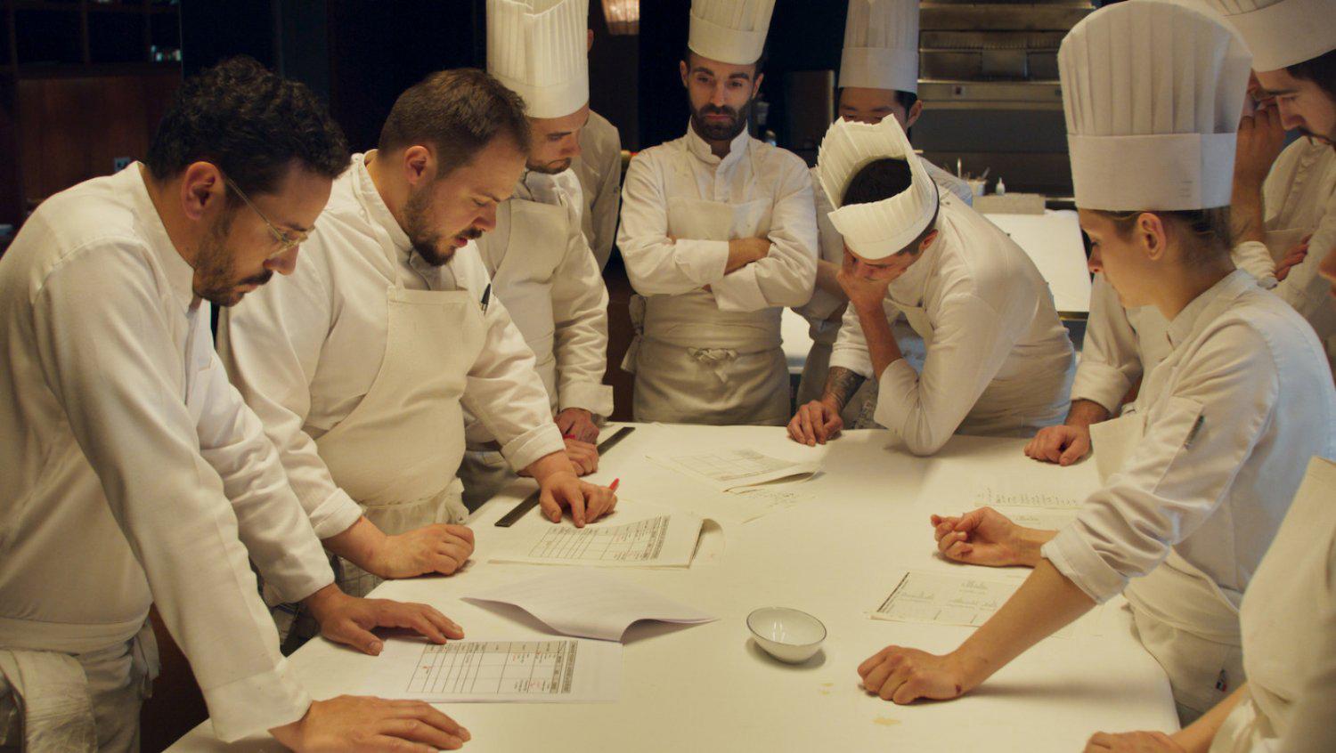Groupe de chefs cuisiniers en vêtements blancs discutant autour d’une table, engrossant des documents.