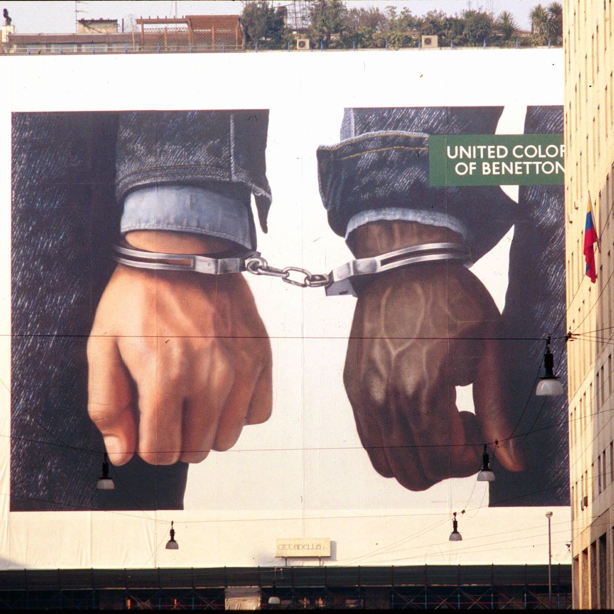 Affiche publicitaire de Benetton par Oliviero Toscani à Milan en 1993, montrant deux mains menottées sur le fond d’un bâtiment.