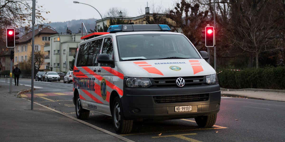 Ein Rettungswagen parkt auf einer Strasse bei einer Ampel, während der Himmel bewölkt ist. Im Hintergrund sind Wohngebäude und Bäume zu sehen.