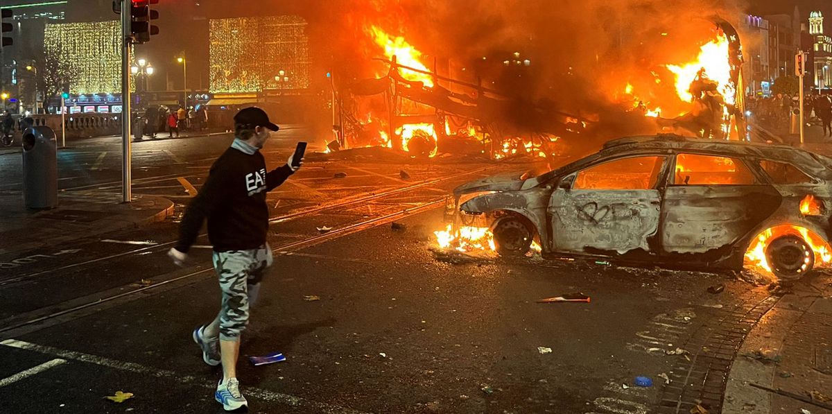 Flames rise from a car and a bus, set alight at the junction of Bachelors Walk and the O'Connell Bridge, in Dublin on November 23, 2023, as people took to the streets in protest following the stabbings earlier in the day. Protesters in Dublin on Thursday torched a car and fought police, an AFP journalist reported, after three children were injured in a suspected school stabbing that social media rumours attributed to a foreign national. (Photo by Peter MURPHY / AFP)
