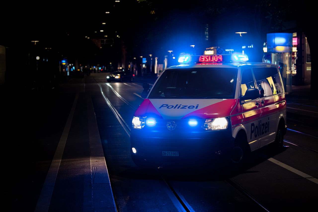 Polizeiwagen mit eingeschaltetem Blaulicht bei Nacht in einer dunklen Strassenumgebung.